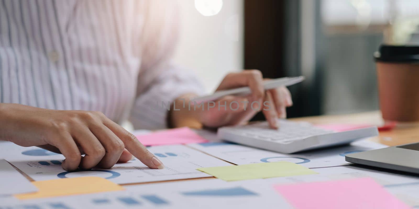 Close up of businesswoman or accountant hand holding pen working on calculator to calculate business data, accountancy document and laptop computer at office, business concept.
