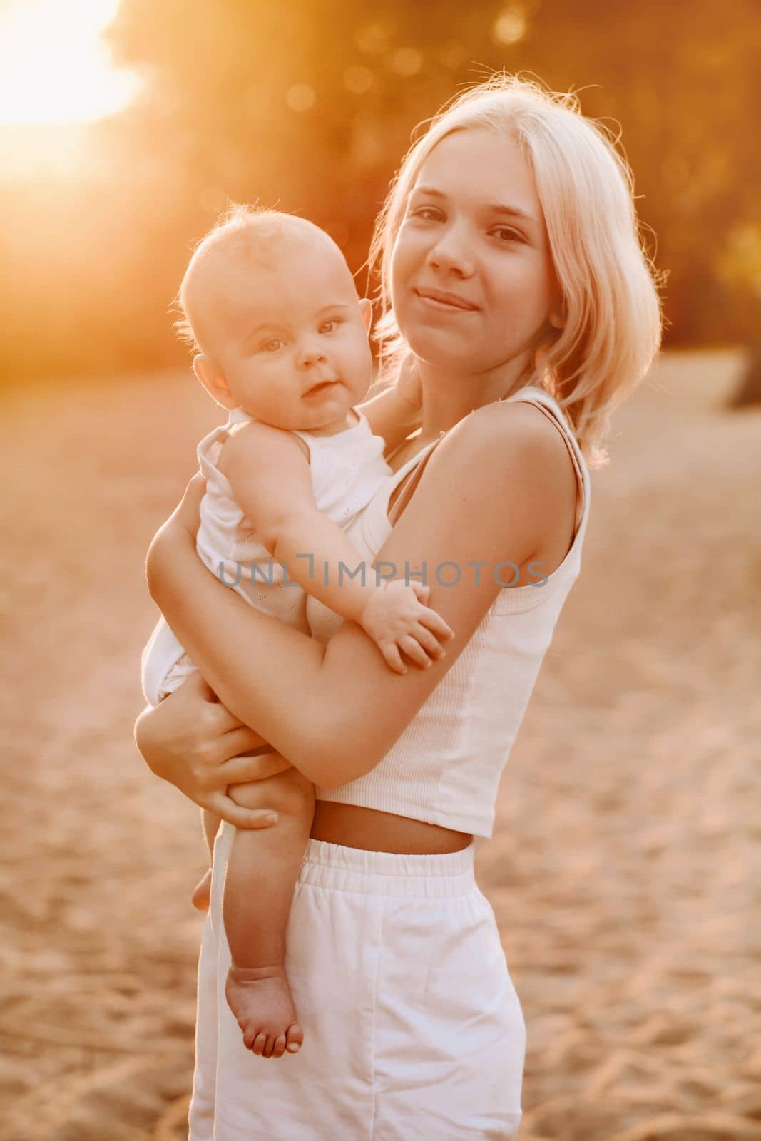 A mother holds a happy baby boy in her arms in a summer park.