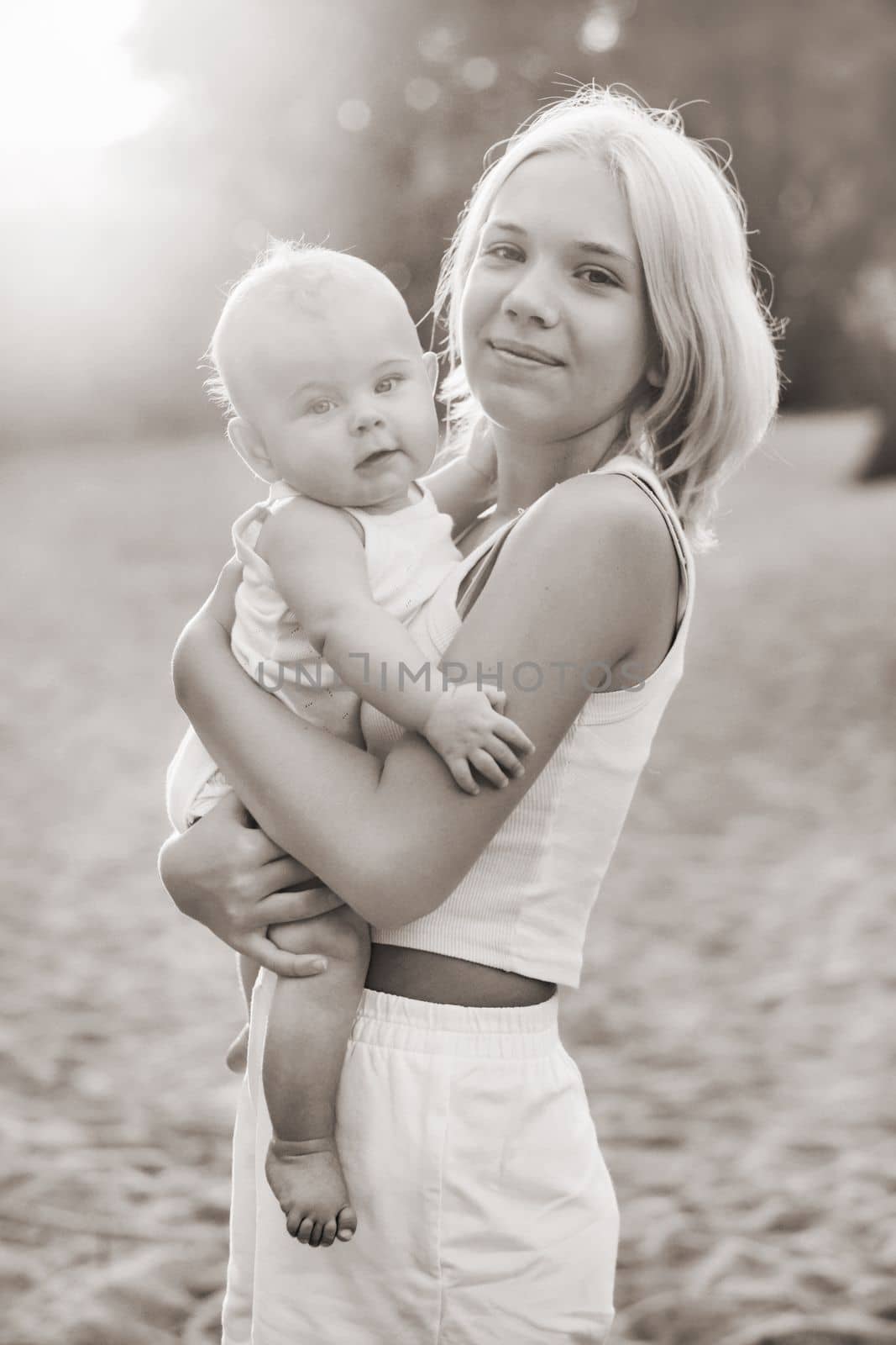 A mother holds a happy baby boy in her arms in a summer park by Lobachad