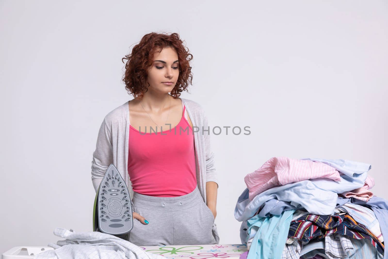 Fresh laundry has arrived on the ironing board in the form of a dozen men's shirts that need to be ironed. The girl is completely deflated and is offended at the whole world.