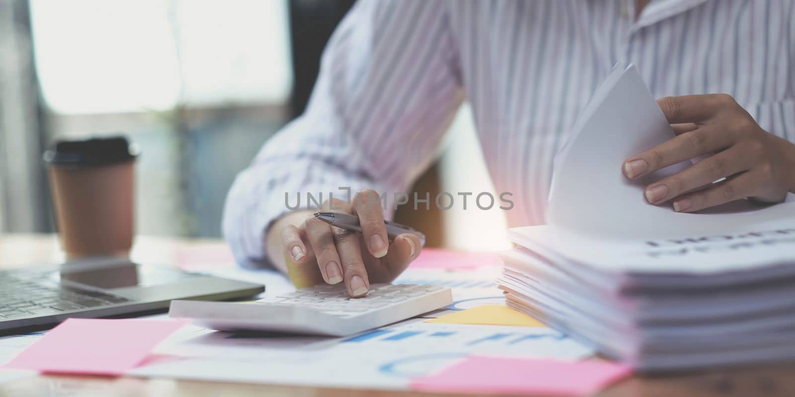 Business woman counting on calculator and holding documents in hands closeup. Bookkeeping concept by wichayada