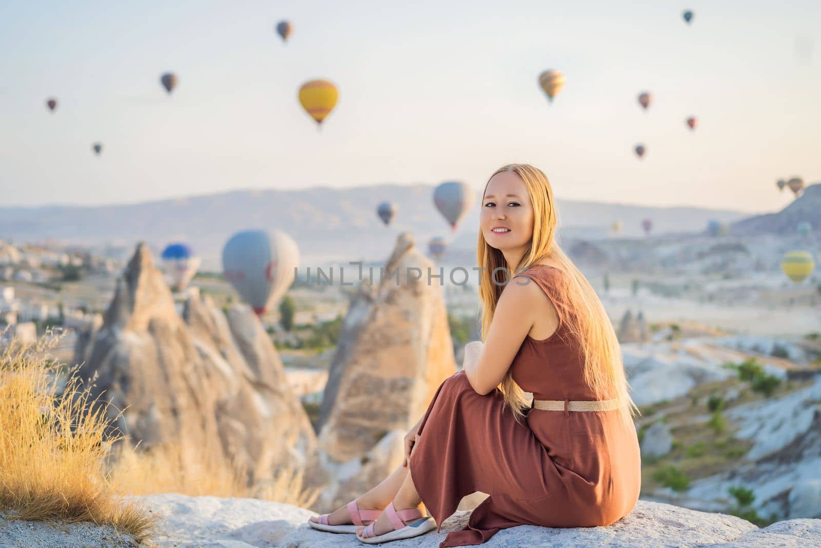 Tourist woman looking at hot air balloons in Cappadocia, Turkey. Happy Travel in Turkey concept. Woman on a mountain top enjoying wonderful view.