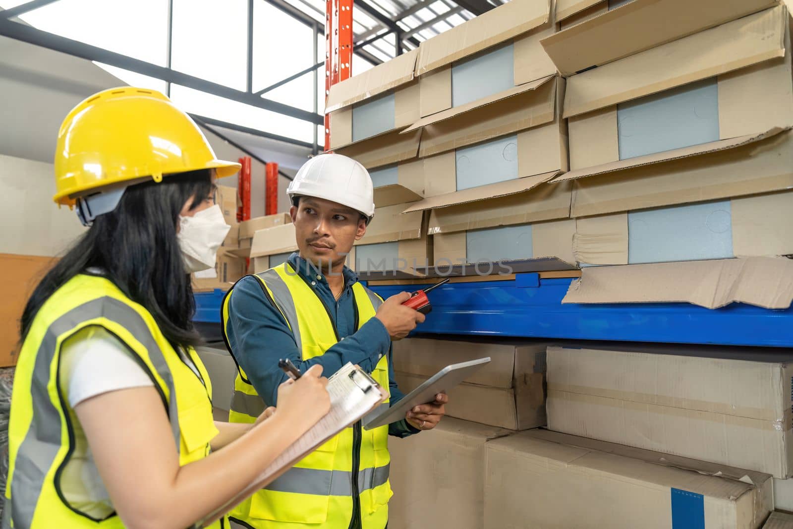 Two smile warehouse workers in uniforms and yellow helmets on heads standing and talking about job. adviser.