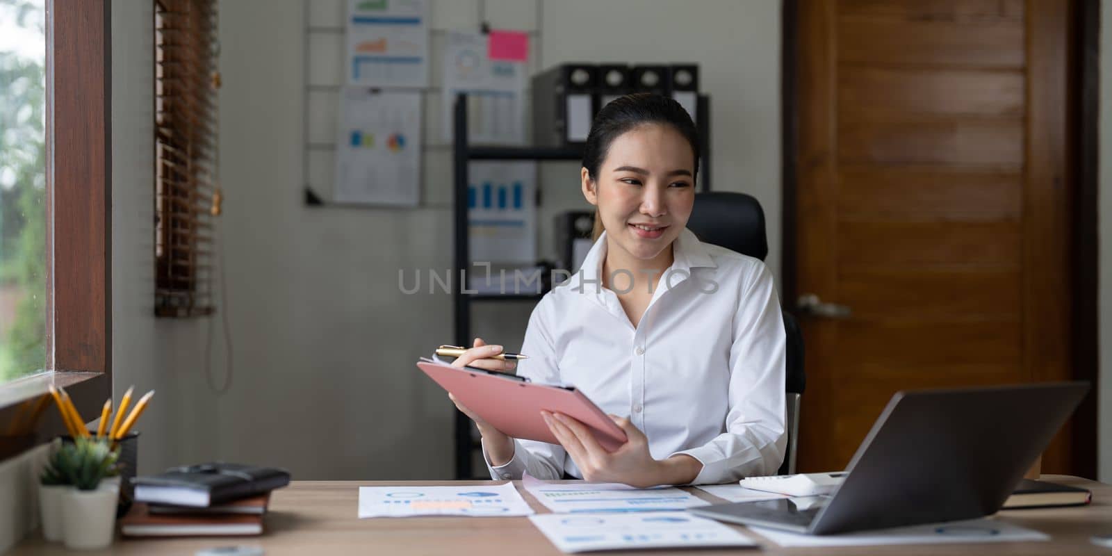 Woman accountant using calculator and laptop computer in office, finance and accounting concept by nateemee