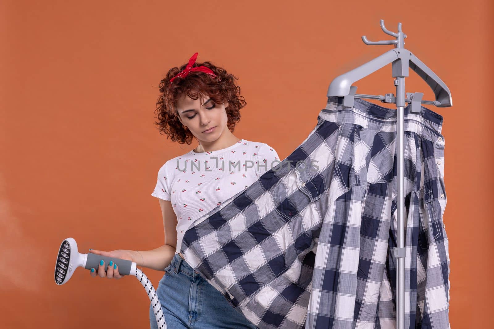 A woman is pondering and bubbling while ironing her shirt. Ironing steamer. Attractive girl with dark and curly hair. Hot steam.