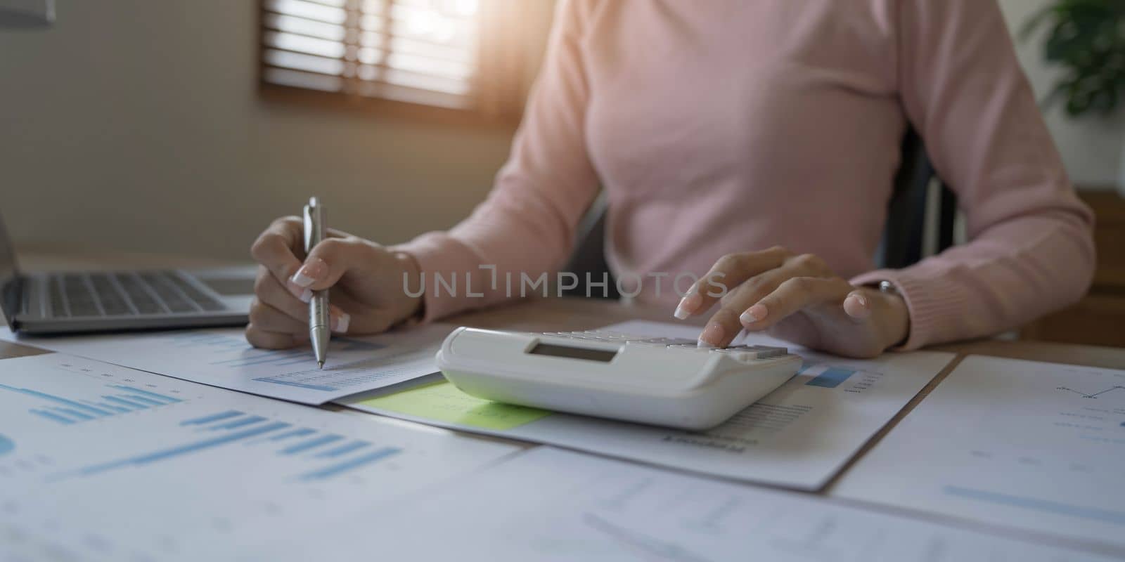 Close up woman or accountant hand working on calculator to calculate business data, accounting document and laptop computer at home by wichayada