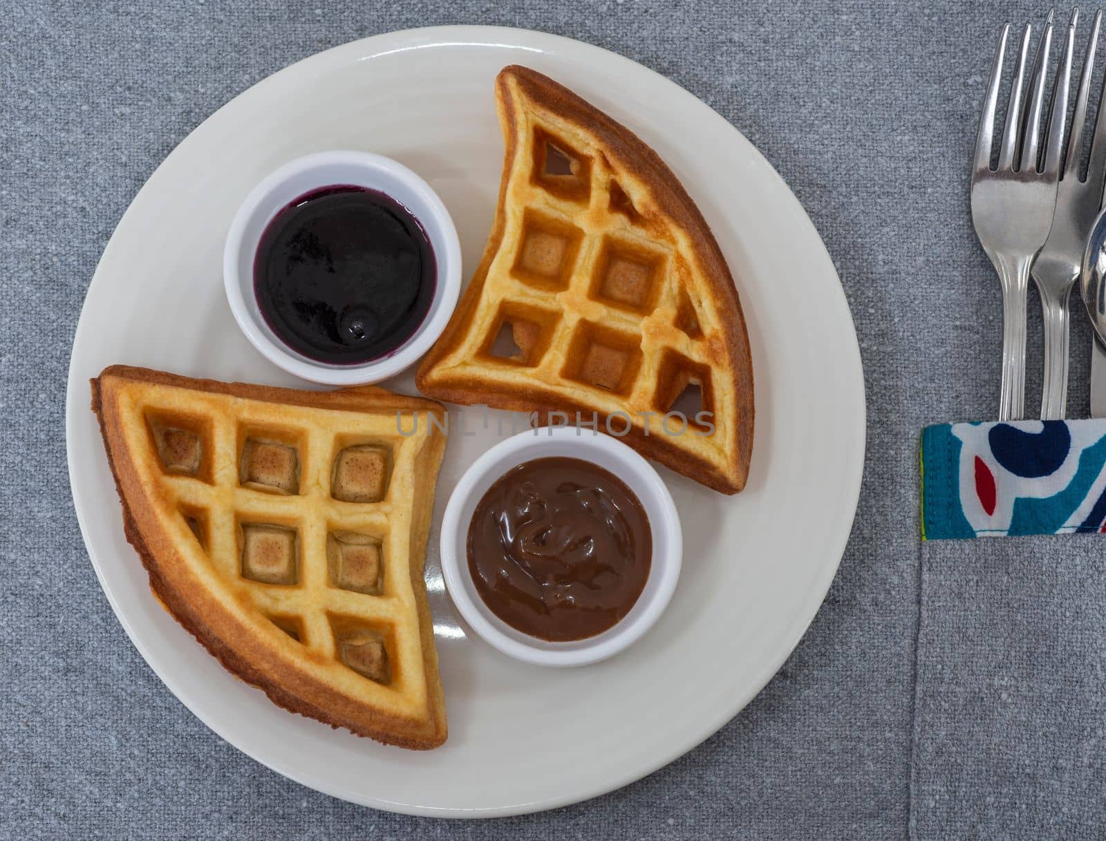 Waffle la carte dessert meal with blueberry and chocolate sauce dips on white plate at restaurant table setting