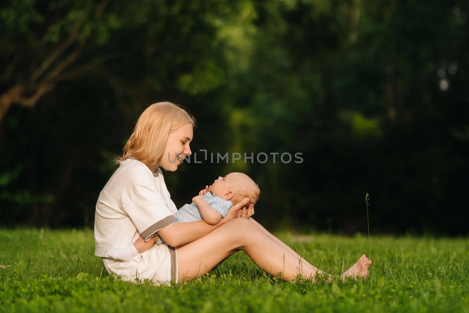 A mother holds a happy baby boy in her arms in a summer park.