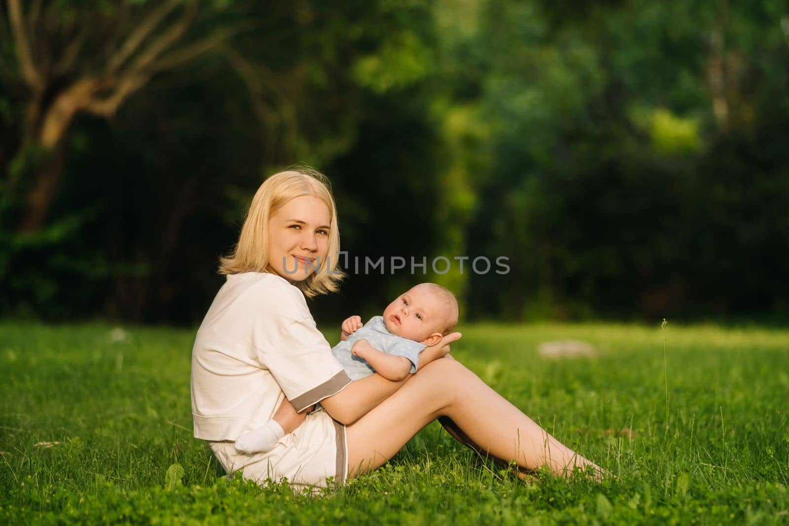 A mother holds a happy baby boy in her arms in a summer park.