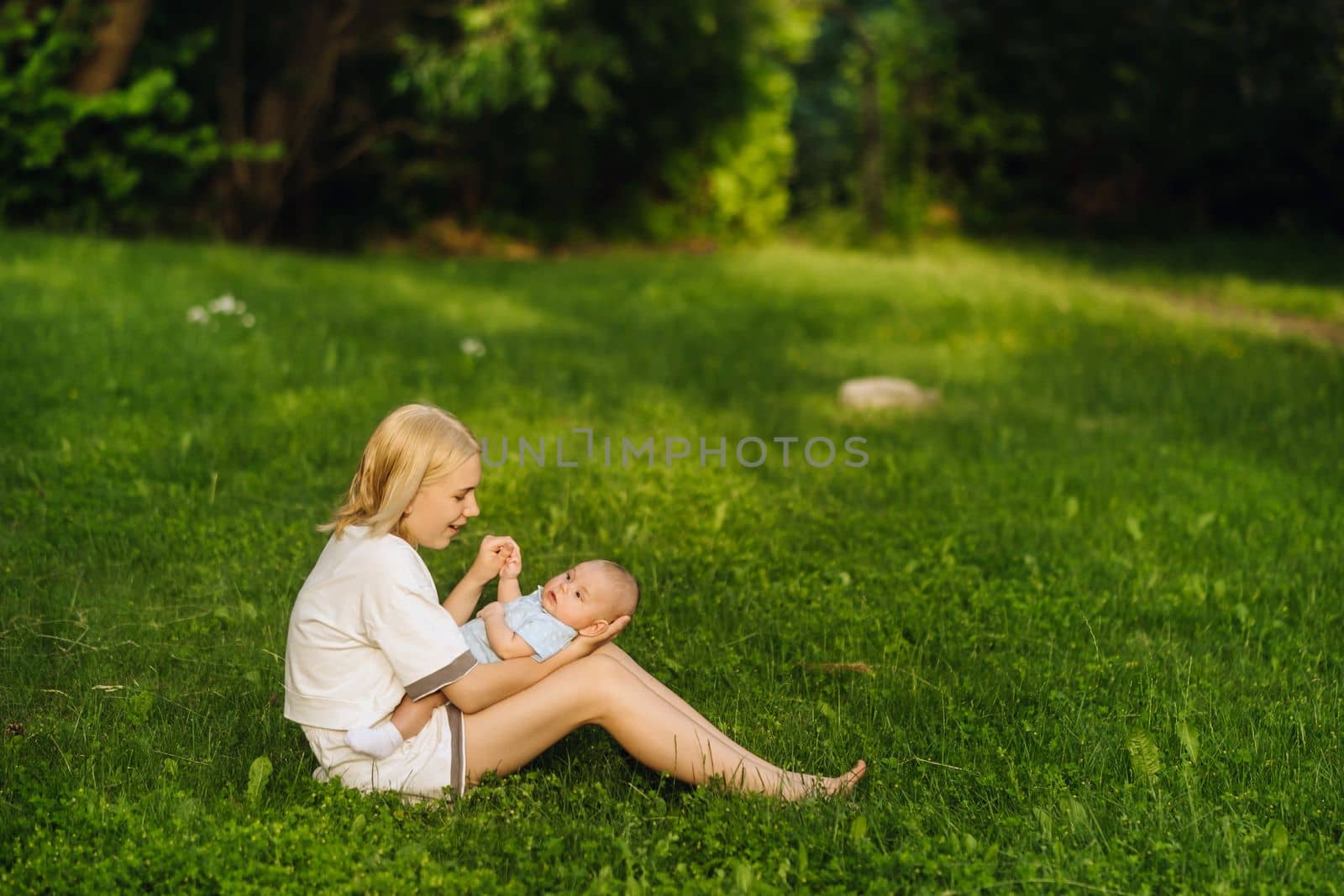 A mother holds a happy baby boy in her arms in a summer park.