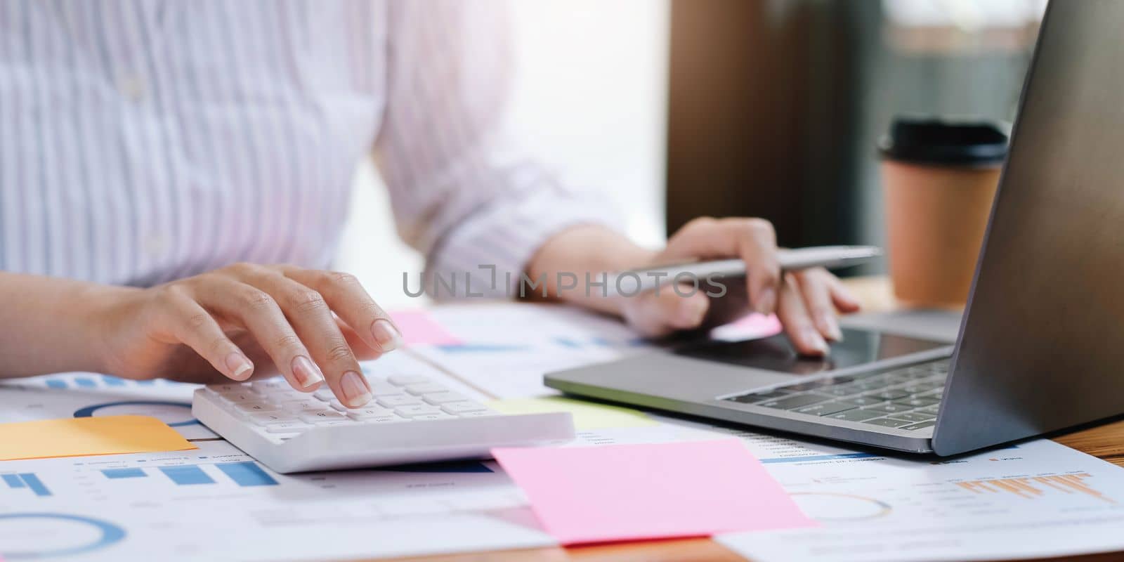 Businesswoman press the white calculator to calculate the numbers in the company financial documents, the finance department prepares the document and forwards it to be checked before the meeting. by wichayada