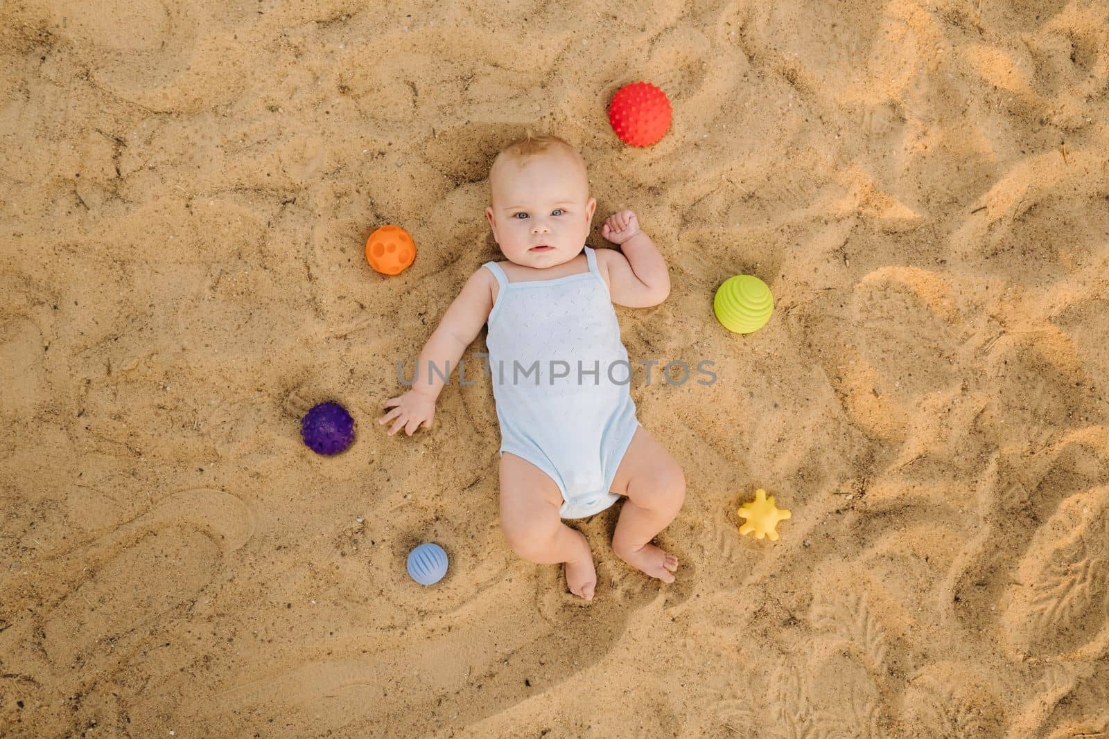 Top view of a happy little boy lying on a sandy beach.