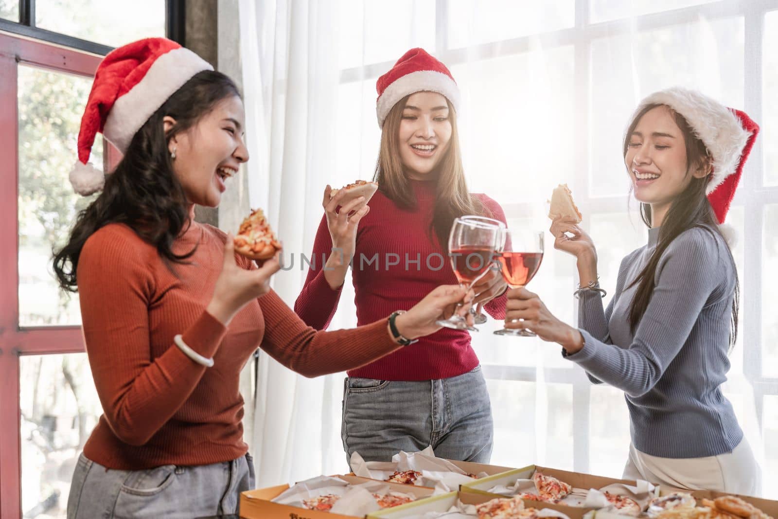 Group of Asian friends gather to celebrate Christmas with champagne and eating pizza at home. Joy of holiday party with friends or colleague concept by nateemee