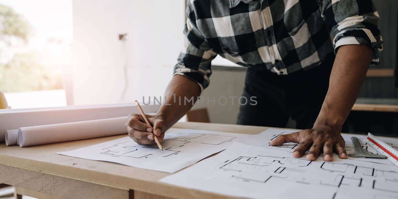 Image of engineer drawing a blue print design building or house, An engineer workplace with blueprints, pencil, protractor and safety helmet, Industry concept by wichayada