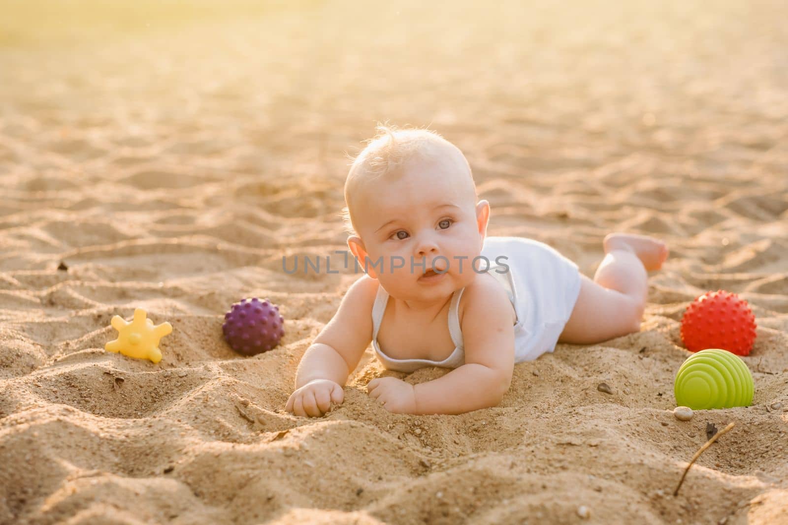 A happy little boy is lying on a sandy beach near the sea in the rays of the setting sun.