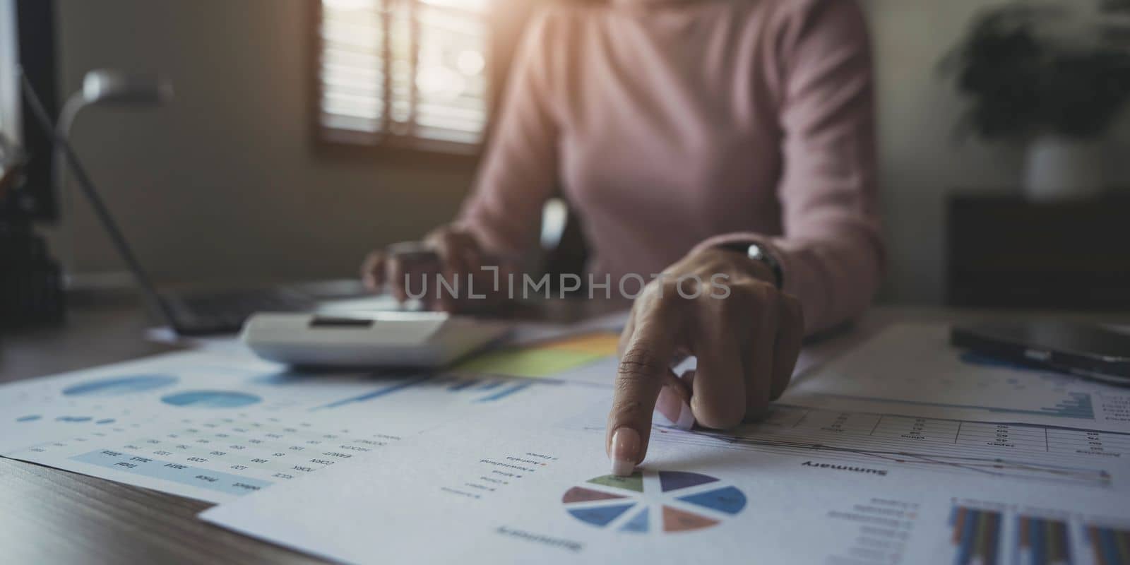 Close up woman or accountant hand working on calculator to calculate business data, accounting document and laptop computer at home by wichayada