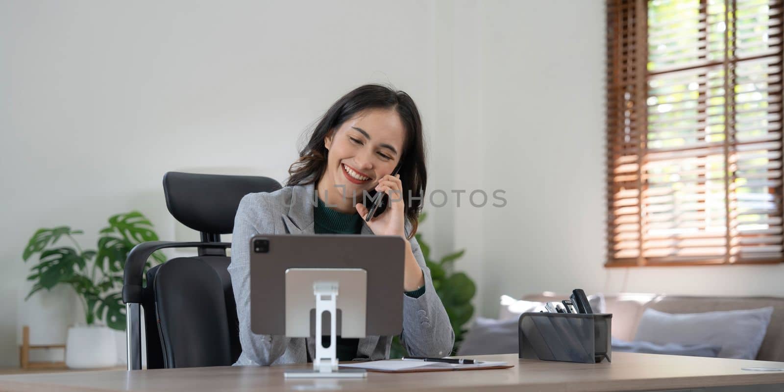 Smiling beautiful Asian businesswoman analyzing chart and graph showing changes on the market and holding smartphone at office...