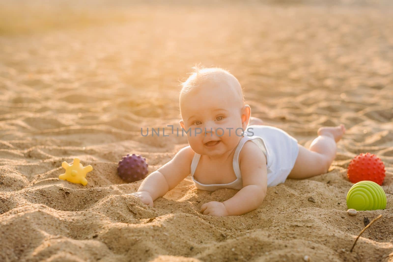 A happy little boy is lying on a sandy beach near the sea in the rays of the setting sun.