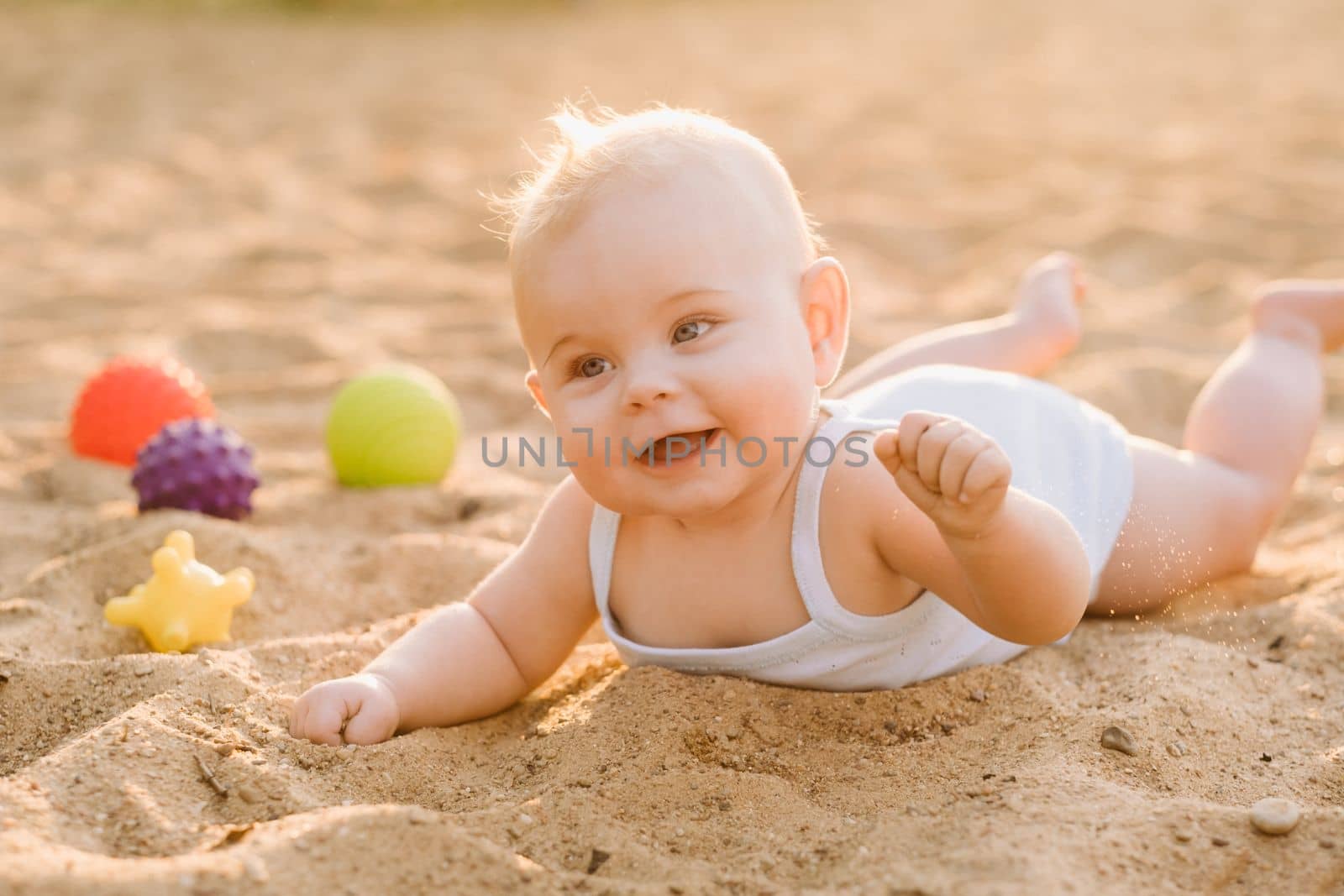 A happy little boy is lying on a sandy beach near the sea in the rays of the setting sun.