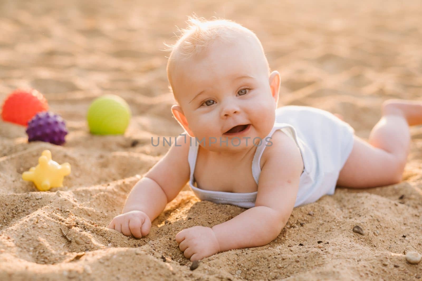 A happy little boy is lying on a sandy beach near the sea in the rays of the setting sun.