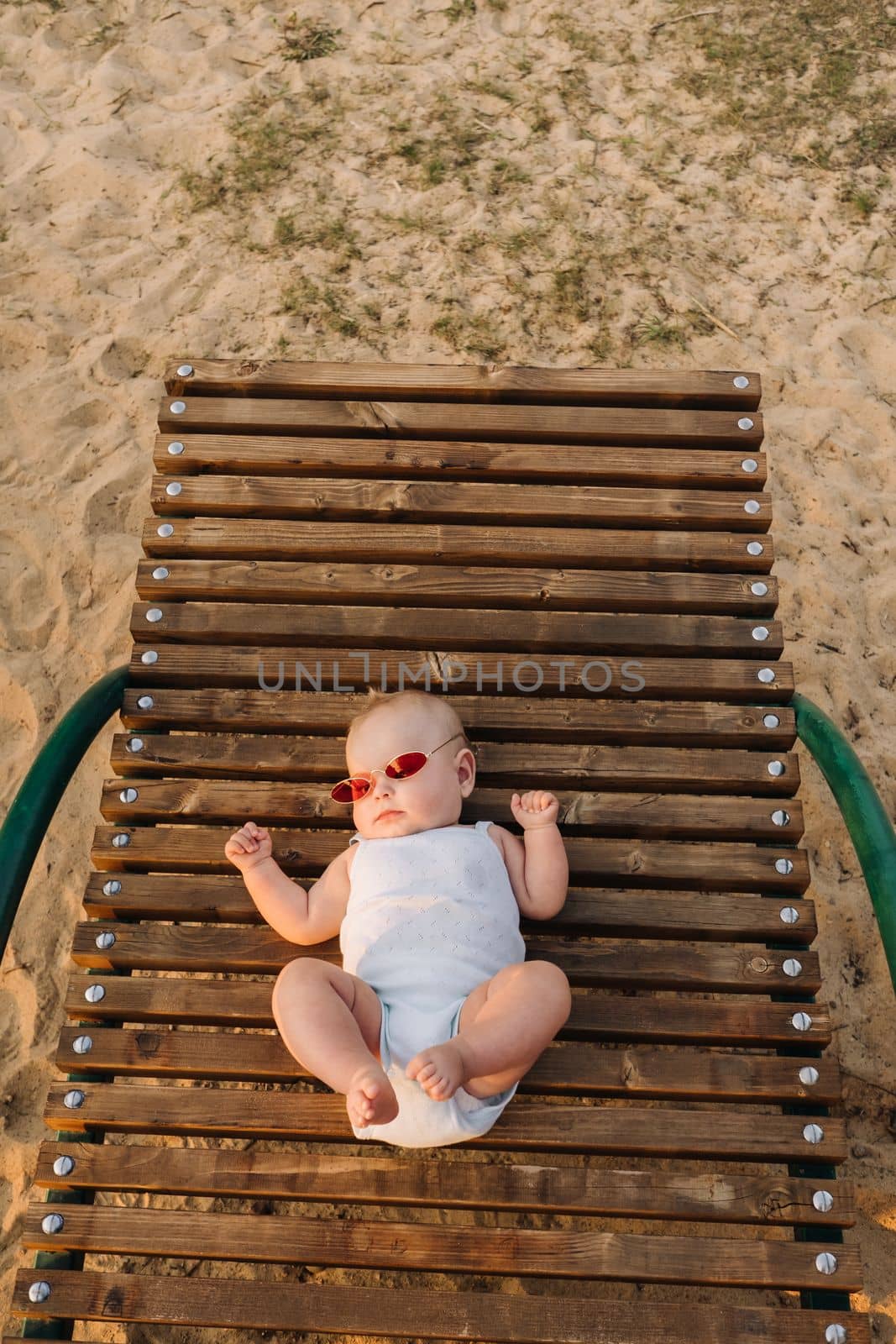 Top view of a happy little boy with glasses lying on a wooden sunbed by Lobachad