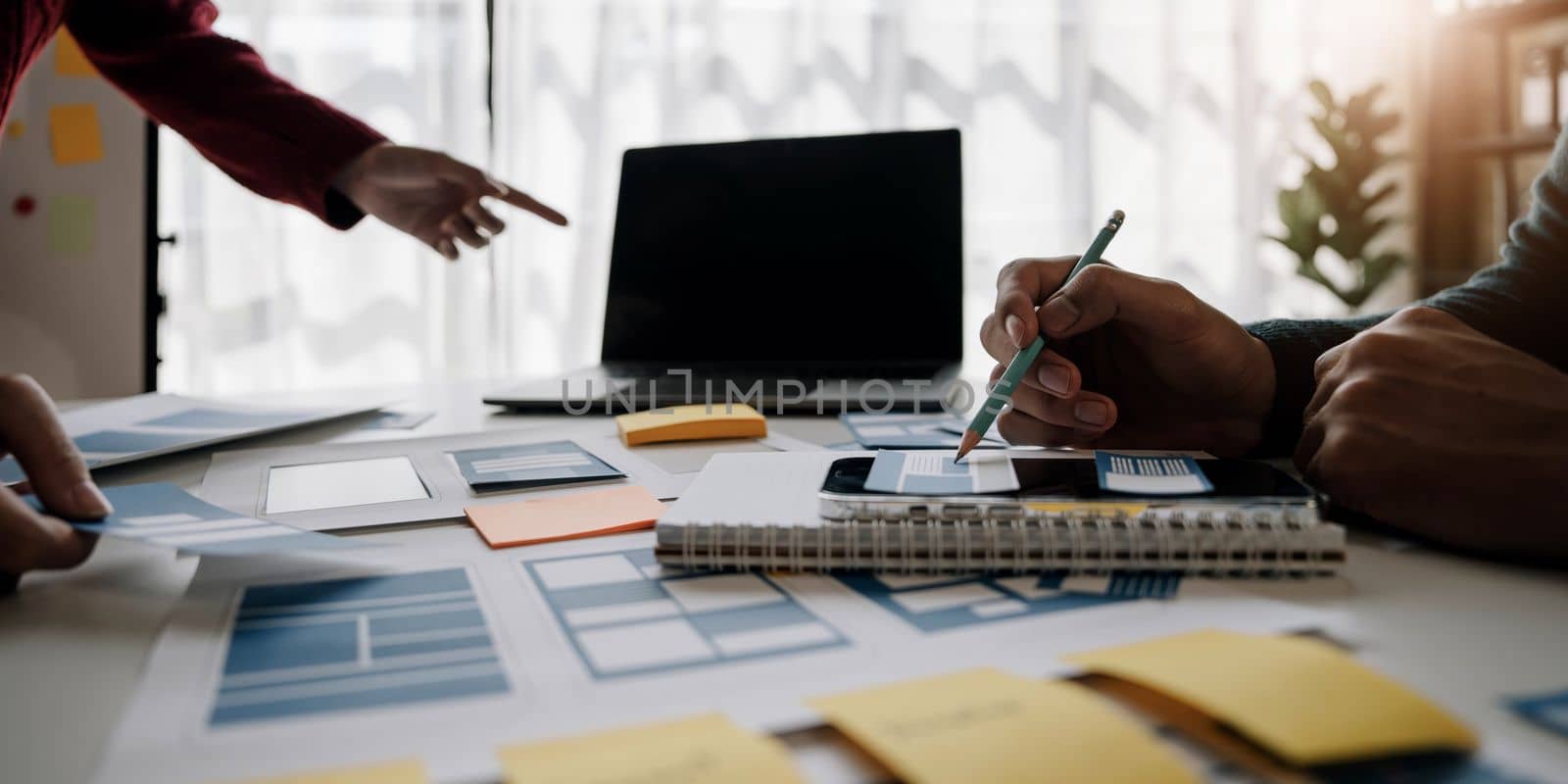 Close up ux developer and ui designer brainstorming about mobile app interface wireframe design on table with customer breif and color code at modern office.Creative digital development agency by wichayada