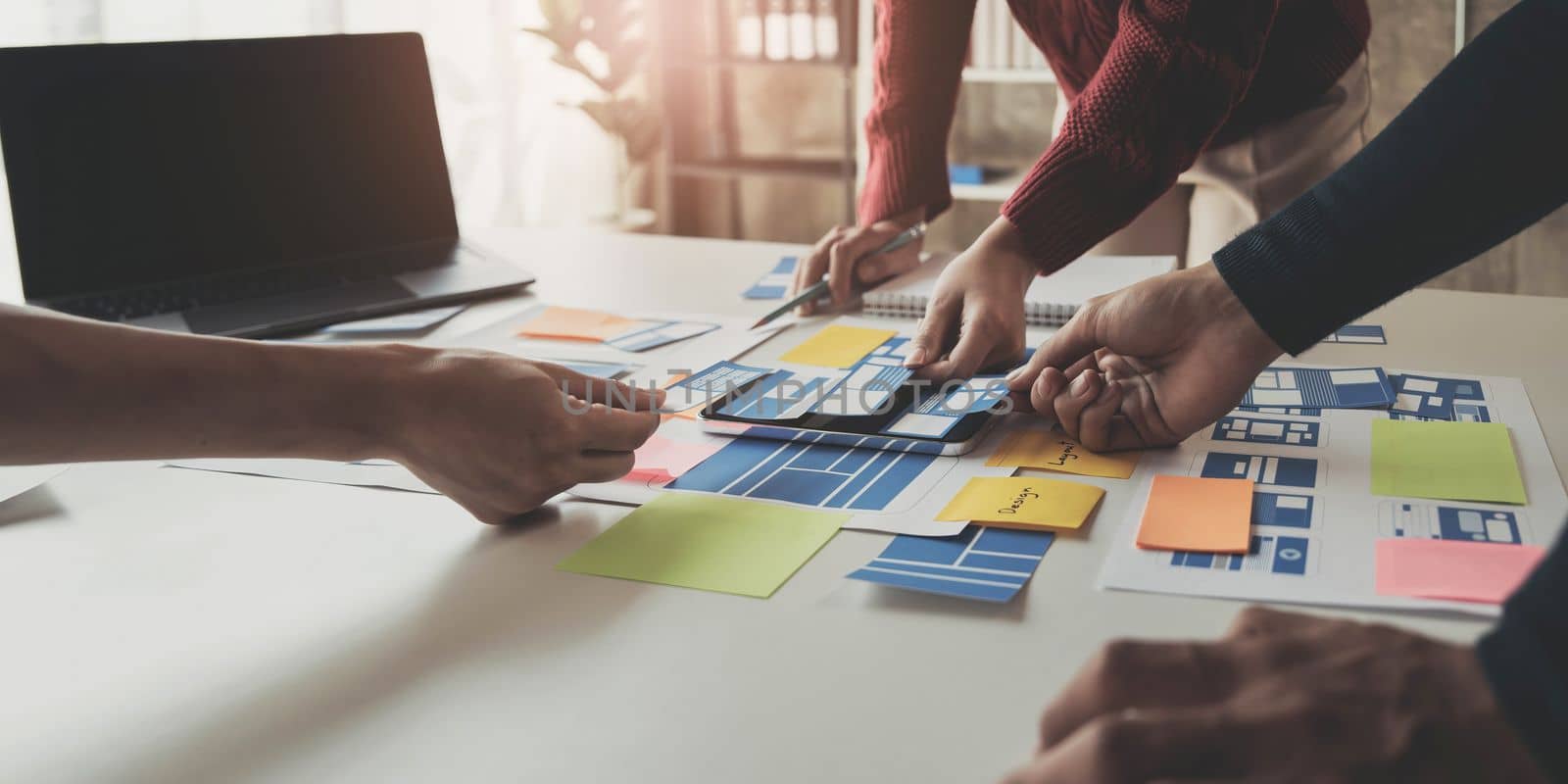 Close up ux developer and ui designer brainstorming about mobile app interface wireframe design on table with customer breif and color code at modern office.Creative digital development agency by wichayada