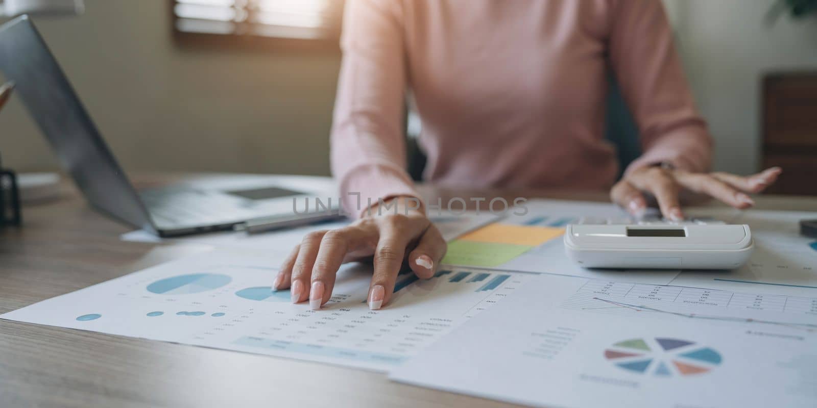 Close up woman or accountant hand working on calculator to calculate business data, accounting document and laptop computer at home by wichayada