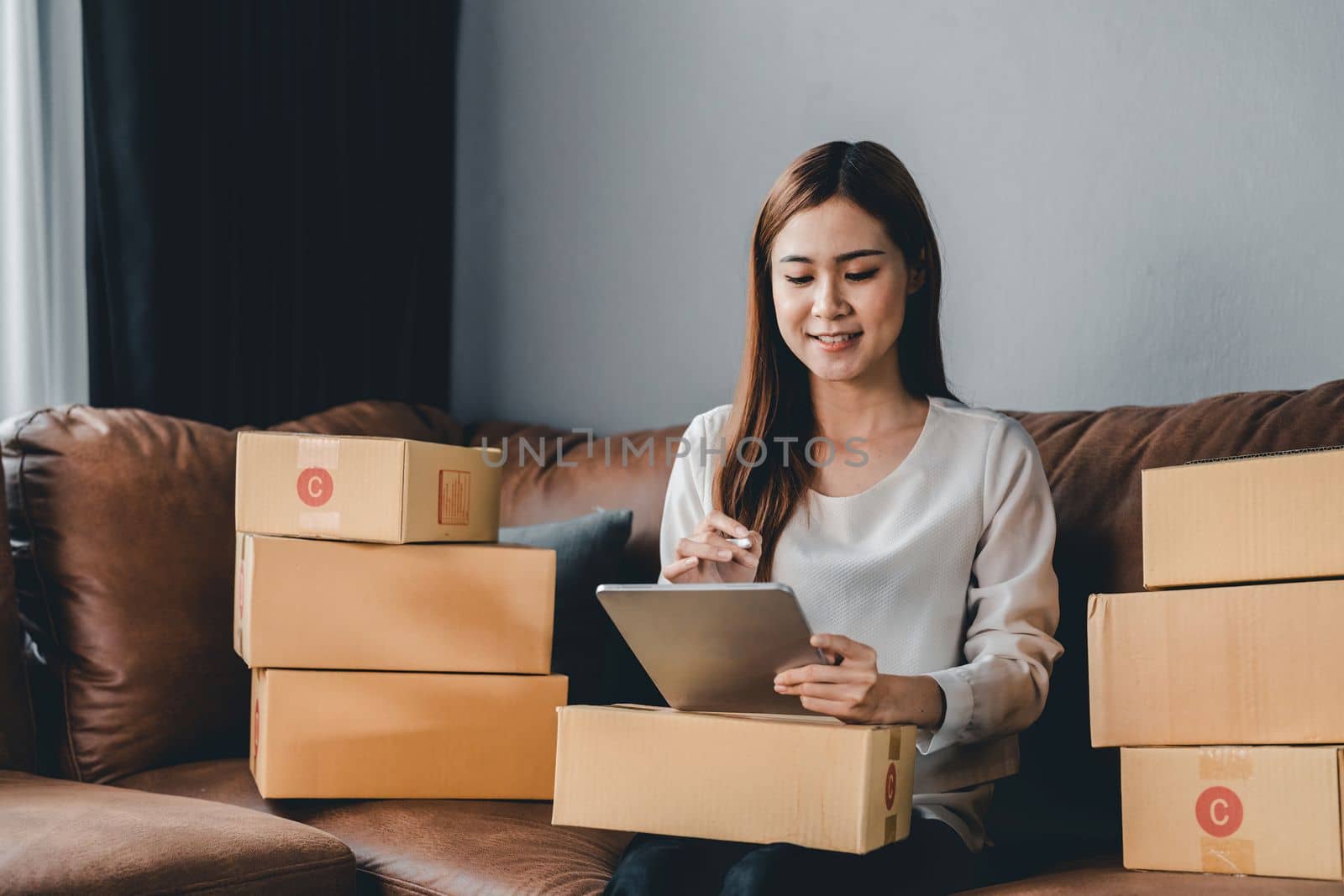 Asian female with small stock business owner holding digital tablet and retail package parcel boxes checking commercial shipping delivery order 