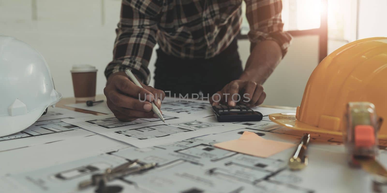 Image of engineer drawing a blue print design building or house, An engineer workplace with blueprints, pencil, protractor and safety helmet, Industry concept..