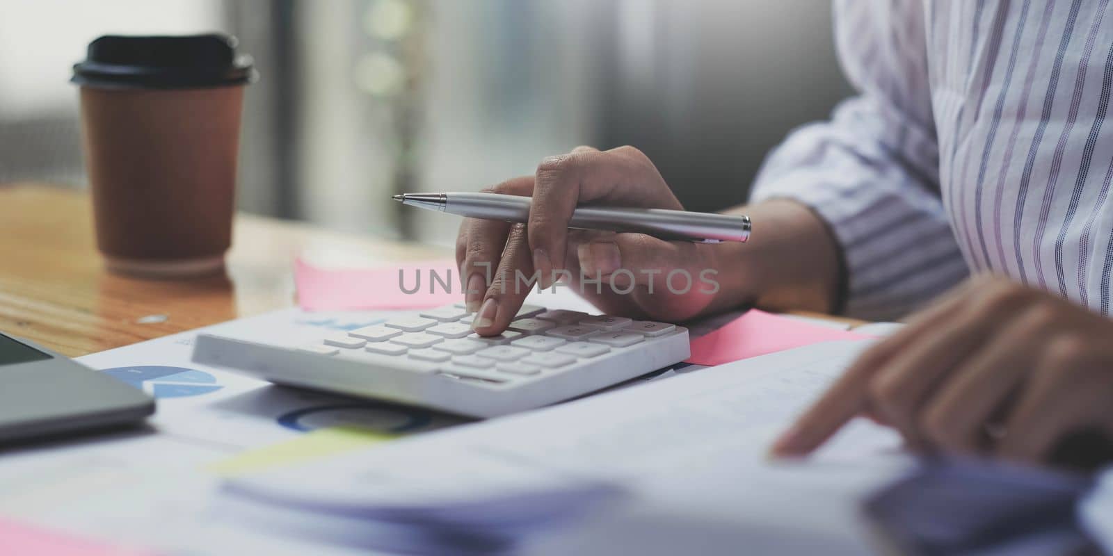 Close up of businesswoman or accountant hand holding pen working on calculator to calculate business data, accountancy document and laptop computer at office, business concept by wichayada