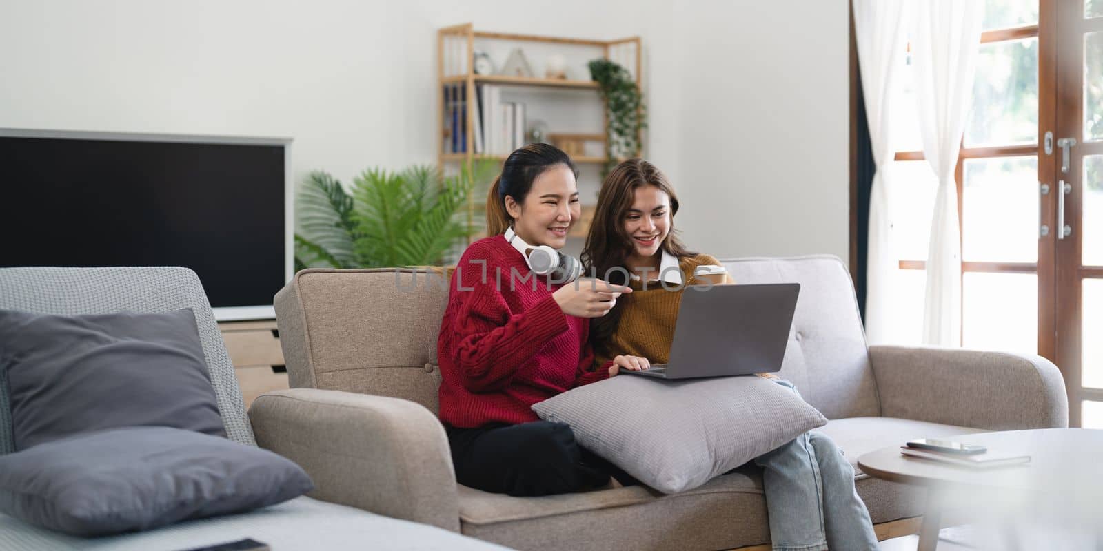 Asian woman friends sitting in living room watching movie on laptop together. Modern female friendship enjoy weekend activity lifestyle with wireless technology at home. by nateemee