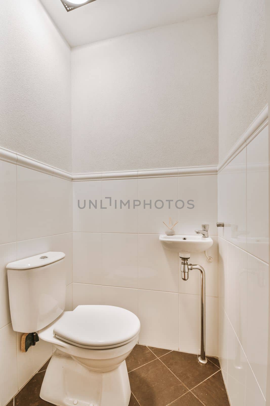 Interior of narrow restroom with sink and wall hung toilet with white walls and checkered floor