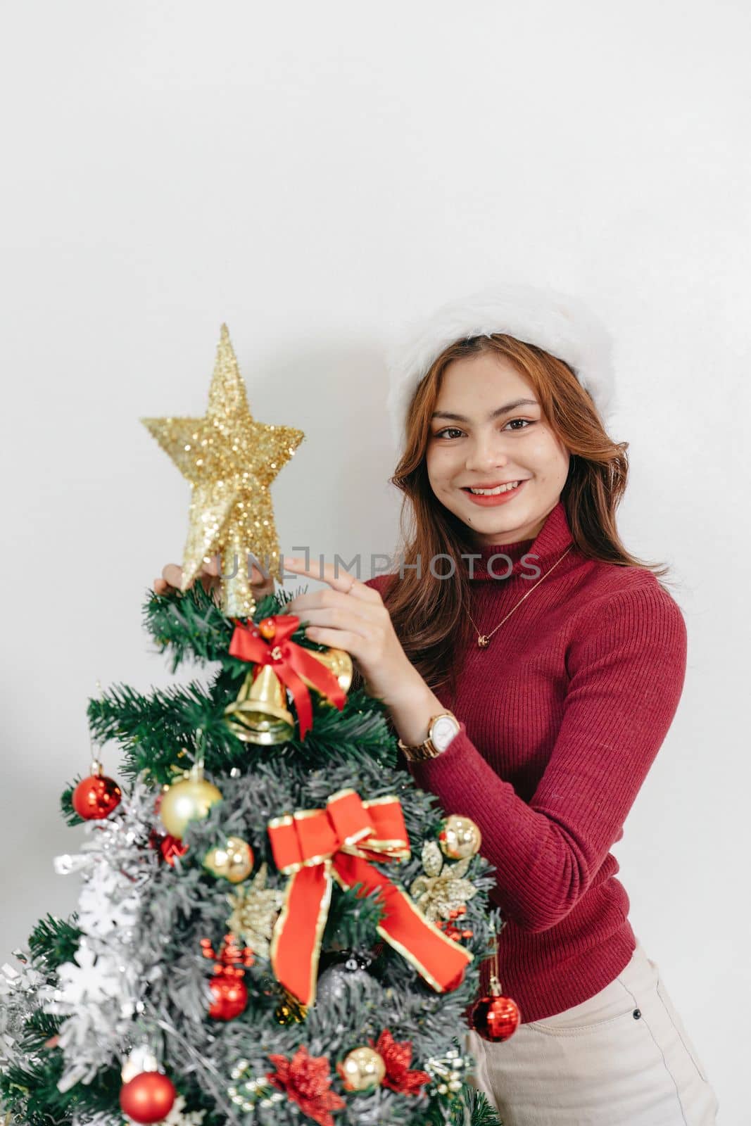 Decorating a Christmas tree. Young woman decorate the Christmas tree in living room at cozy home by nateemee