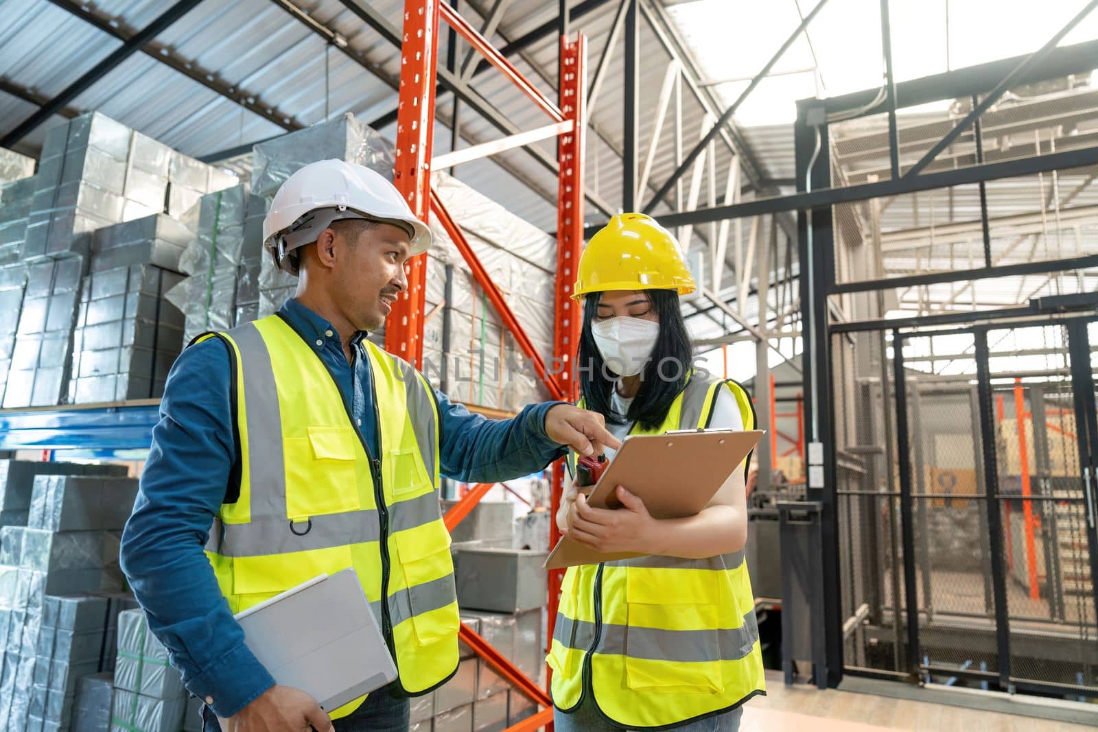 Two smile warehouse workers in uniforms and yellow helmets on heads standing and talking about job. adviser.