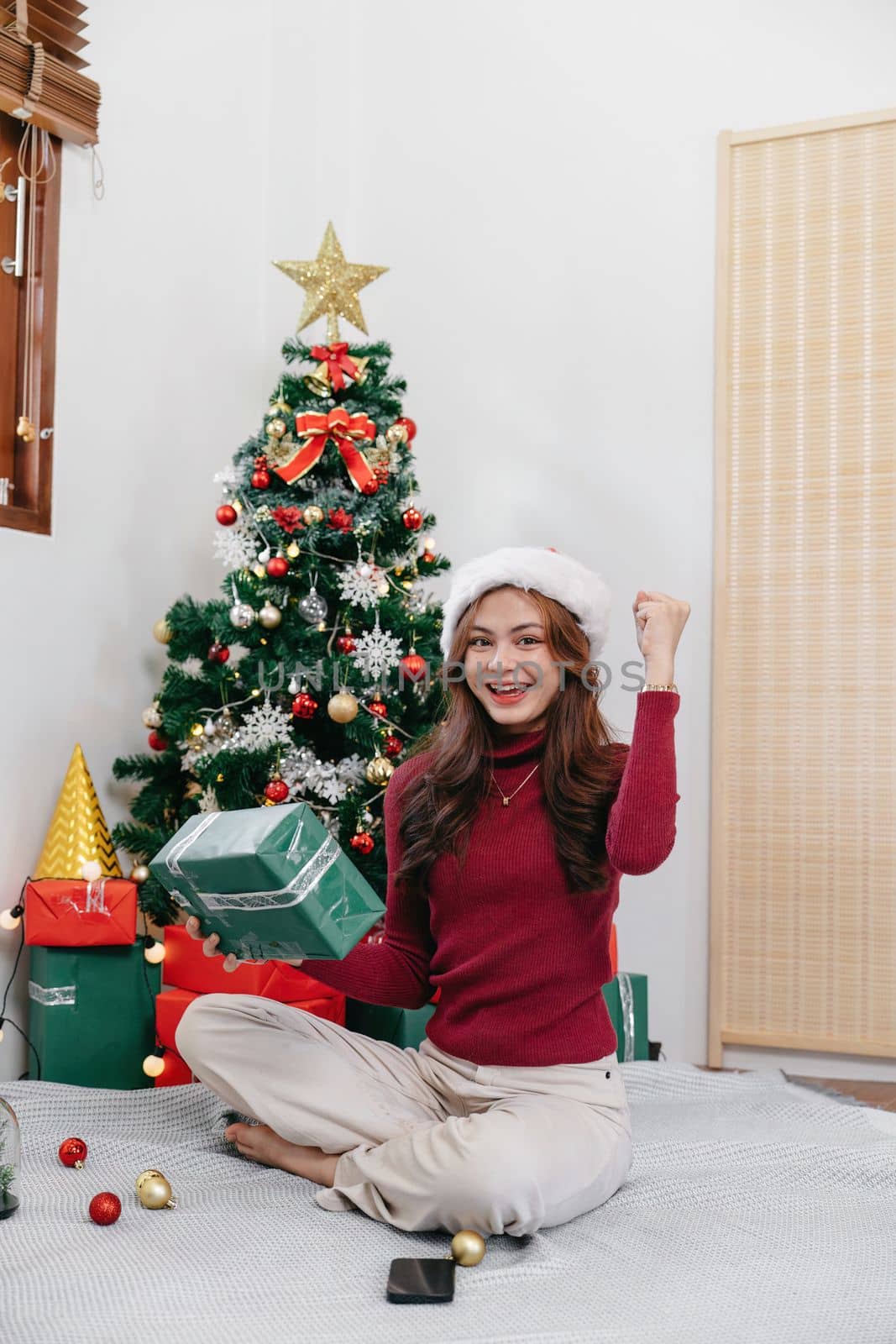 Happy woman sitting against Christmas tree background. Cheerful lady surprised of gift box. Marry Christmas and Happy Holidays by nateemee