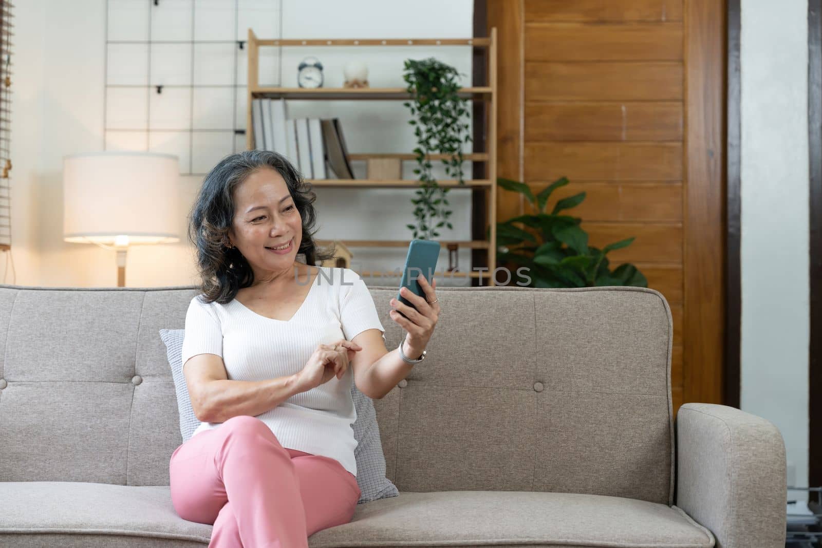 Smiling senior lady using her smartphone, she is connecting online and using apps at cozy home by nateemee