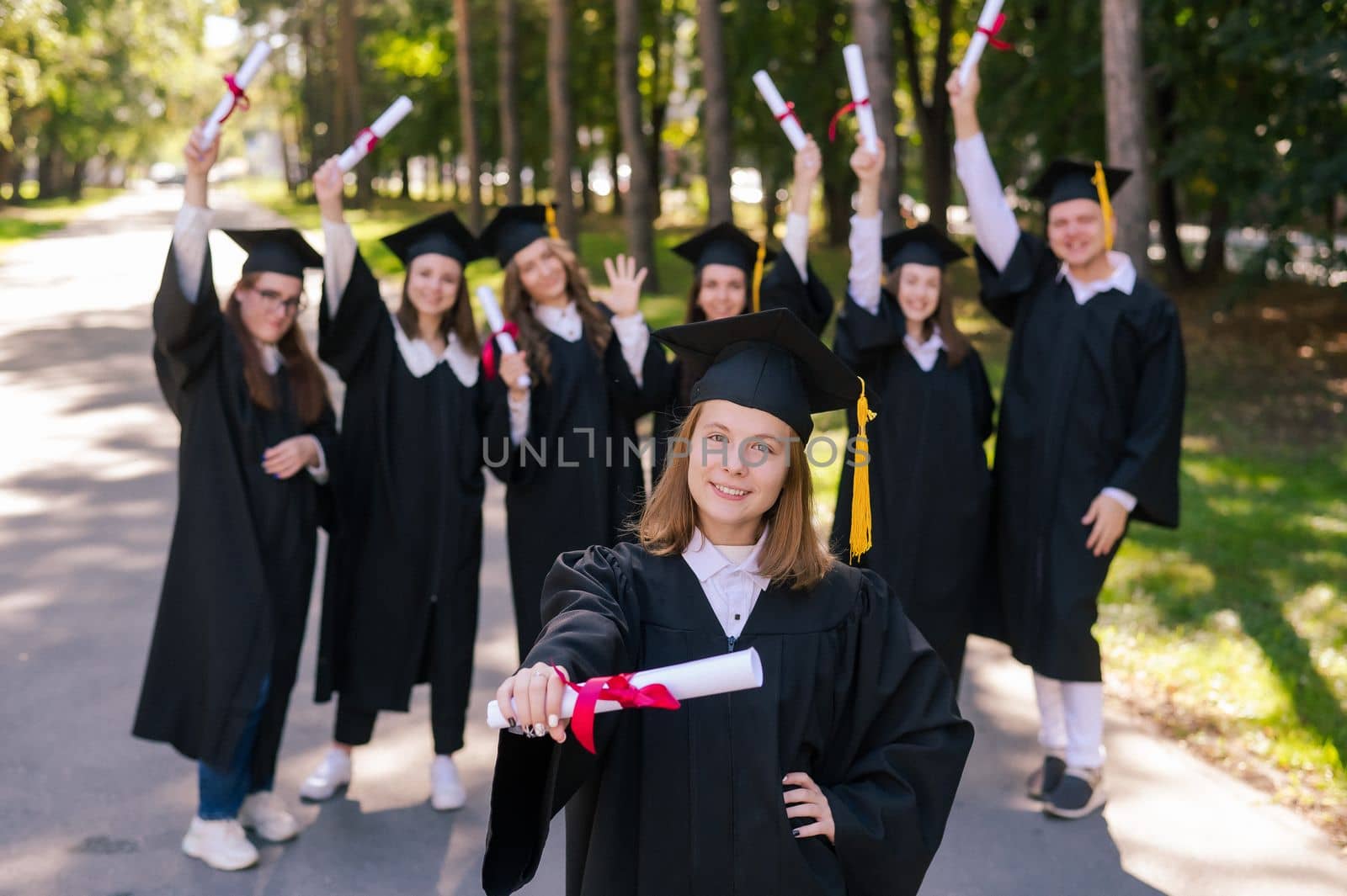 Happy young caucasian woman celebrating graduation with classmates. A group of graduate students outdoors