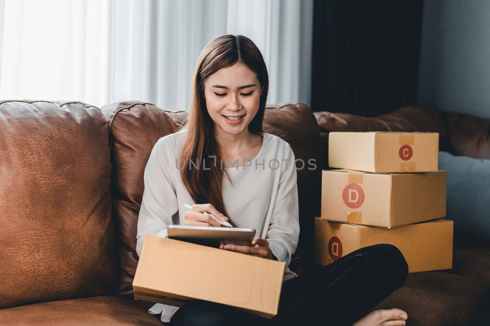 Asian female with small stock business owner holding digital tablet and retail package parcel boxes checking commercial shipping delivery order 