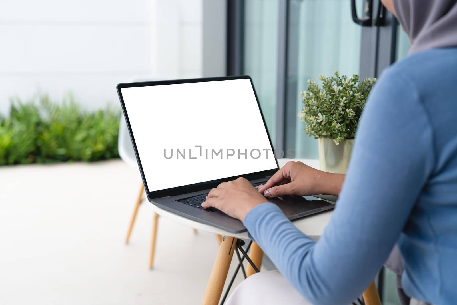 Mockup image of hand using laptop with blank white screen on table. muslim woman with hijab working online from home