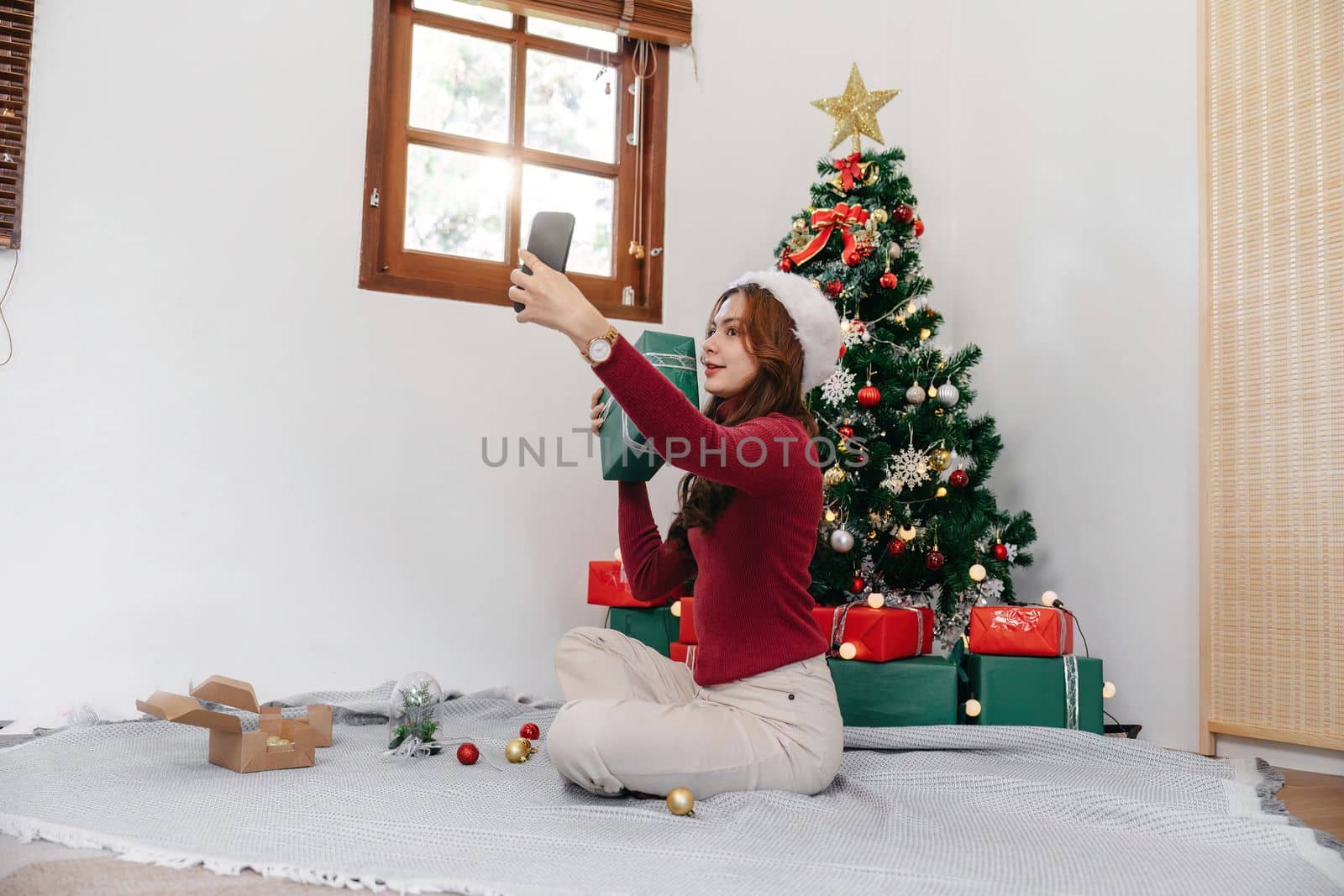 Holiday selfie at Christmas tree. Happy young girl taking selfie on smart phone at decorated Christmas tree iat home.