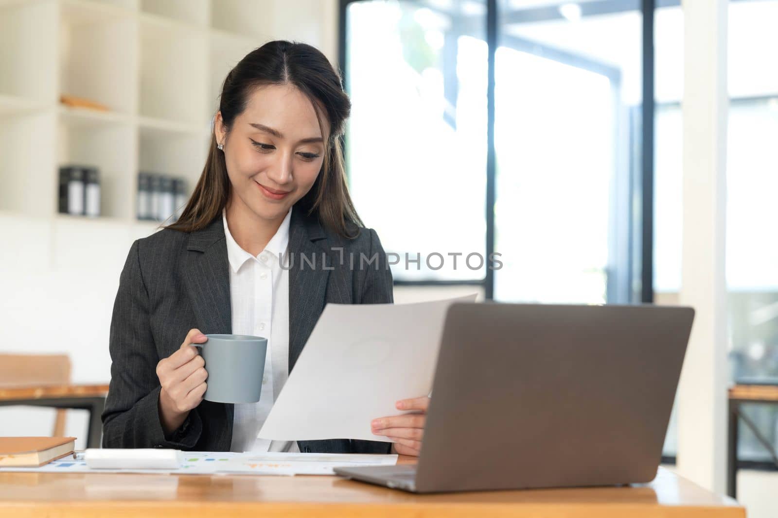 Beautiful young Asian businesswoman smiling holding a coffee mug and laptop working at the office..