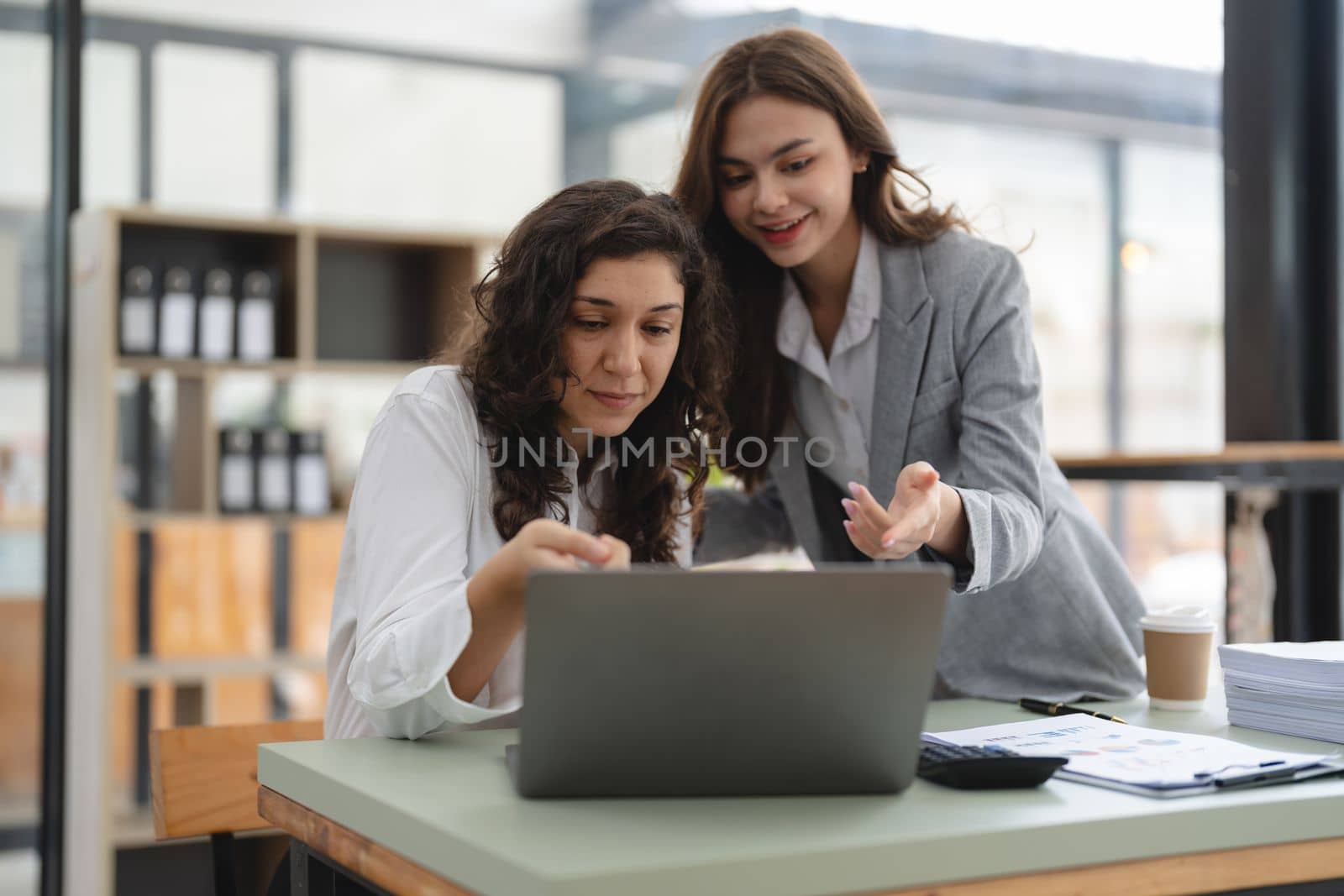 Two smart multiethnic business people working together with laptop while talking about job news in the office