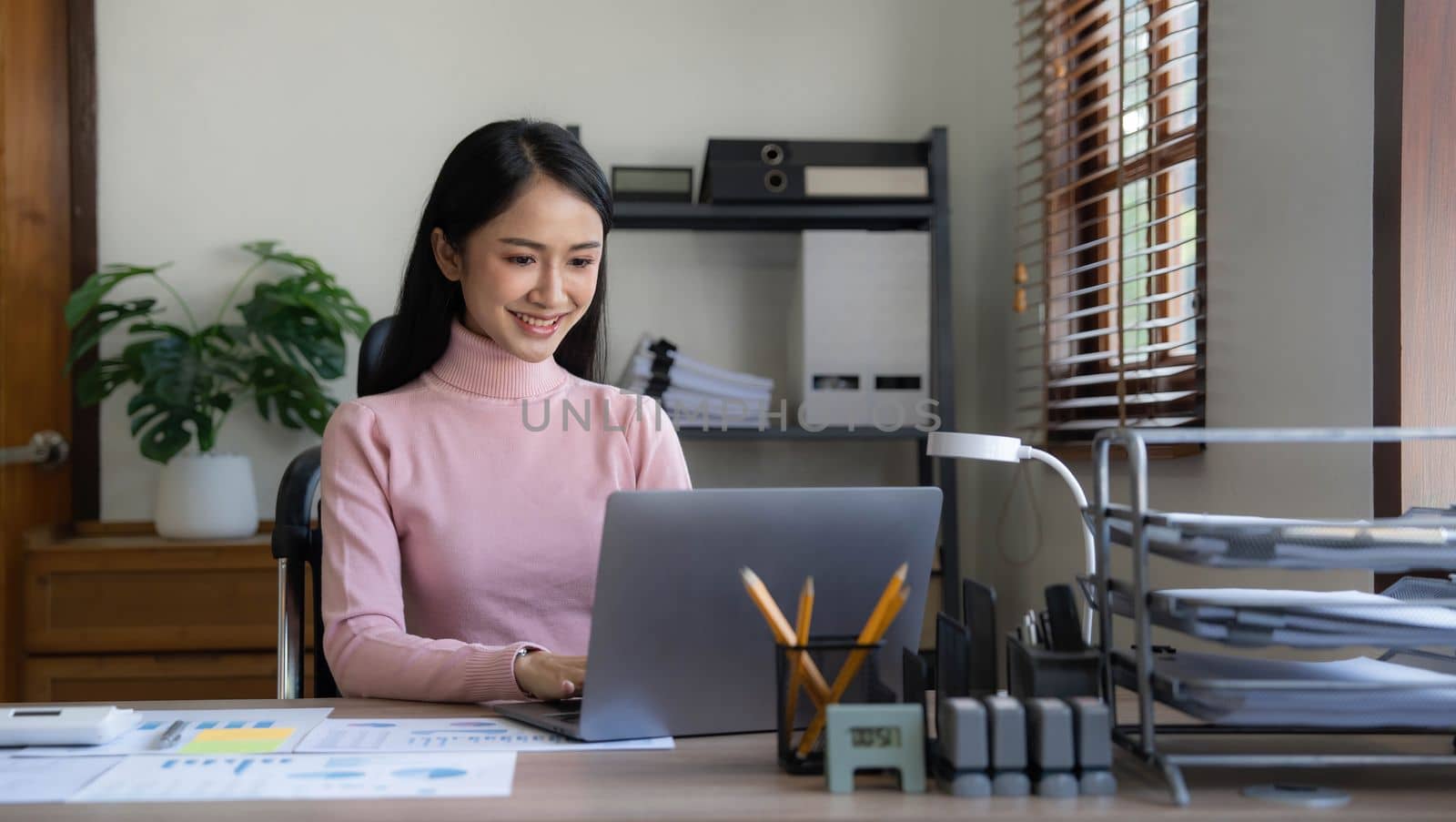 Asian Business woman using calculator and laptop for doing math finance on an office desk, tax, report, accounting, statistics, and analytical research concept by wichayada