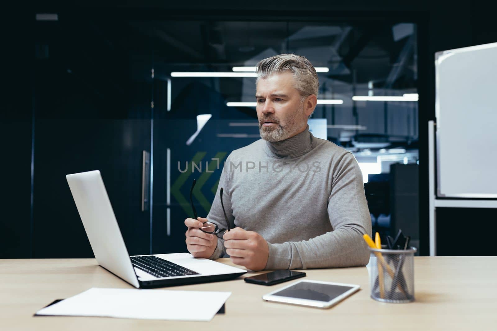 Serious thinking businessman inside office at work with laptop, senior gray haired man working sitting at desk.