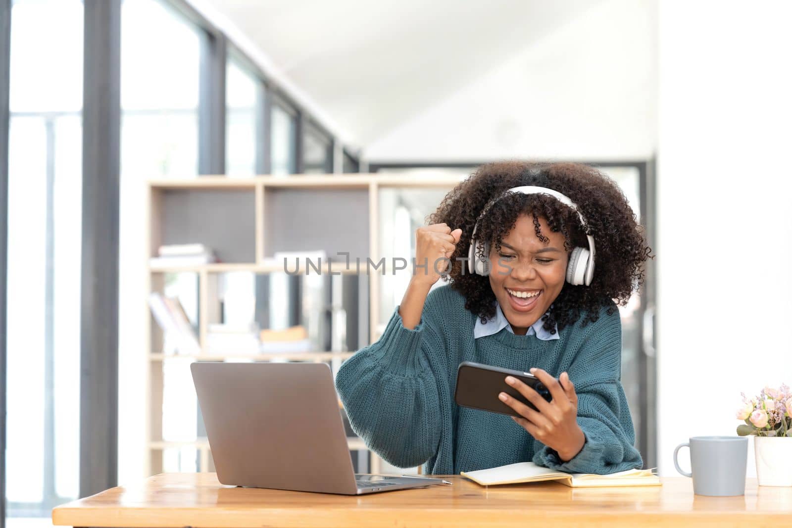 Photo of cheerful joyful mixed race woman playing games and wearing wireless headphones at home Play game on your smartphone that wins the moment of victory. Fun and enjoyable vacation.