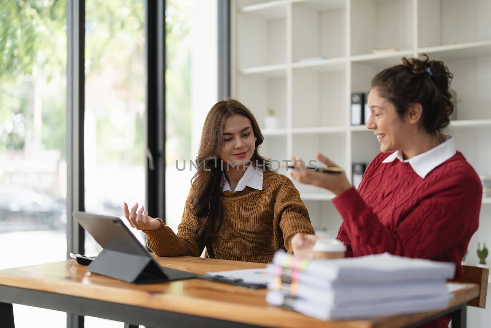 Two multiethnic professionals colleagues working together with laptop and papers in office. Female mentor and young professional sitting in creative office