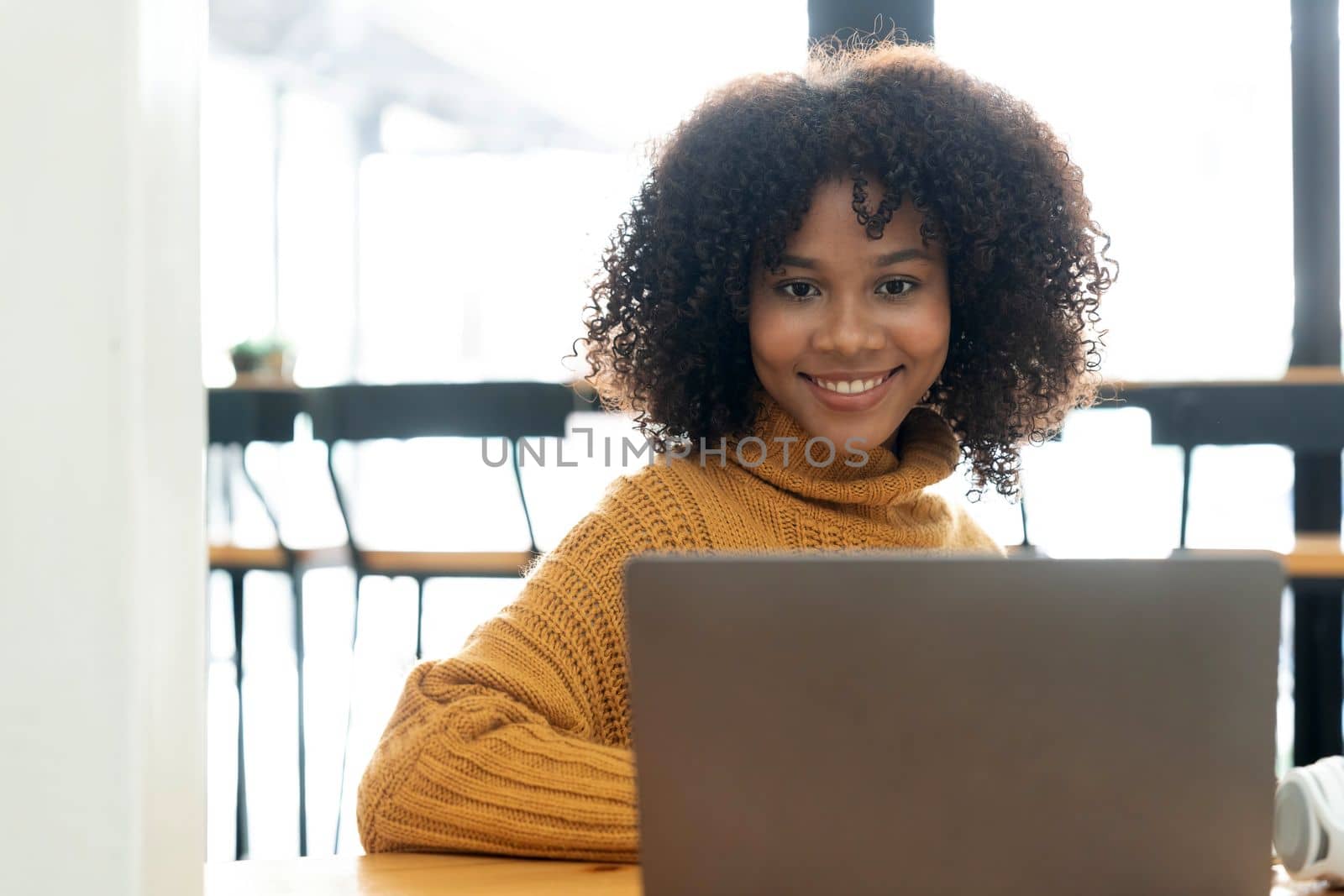 Photo of cheerful joyful mixed race woman in yellow shirt smiling work on laptop talk speak video call online. Smart ethnic female in earphones study distant on computer at home. Education concept...