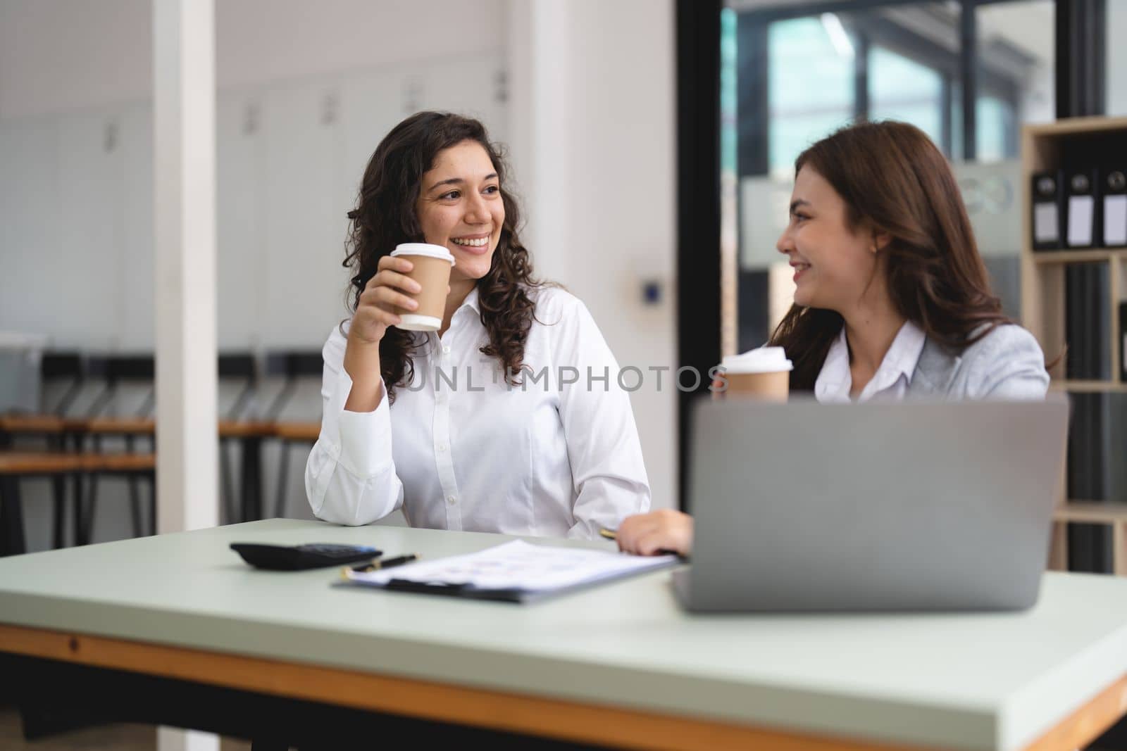 Two smart multiethnic business people working together with laptop while talking about job news in the office