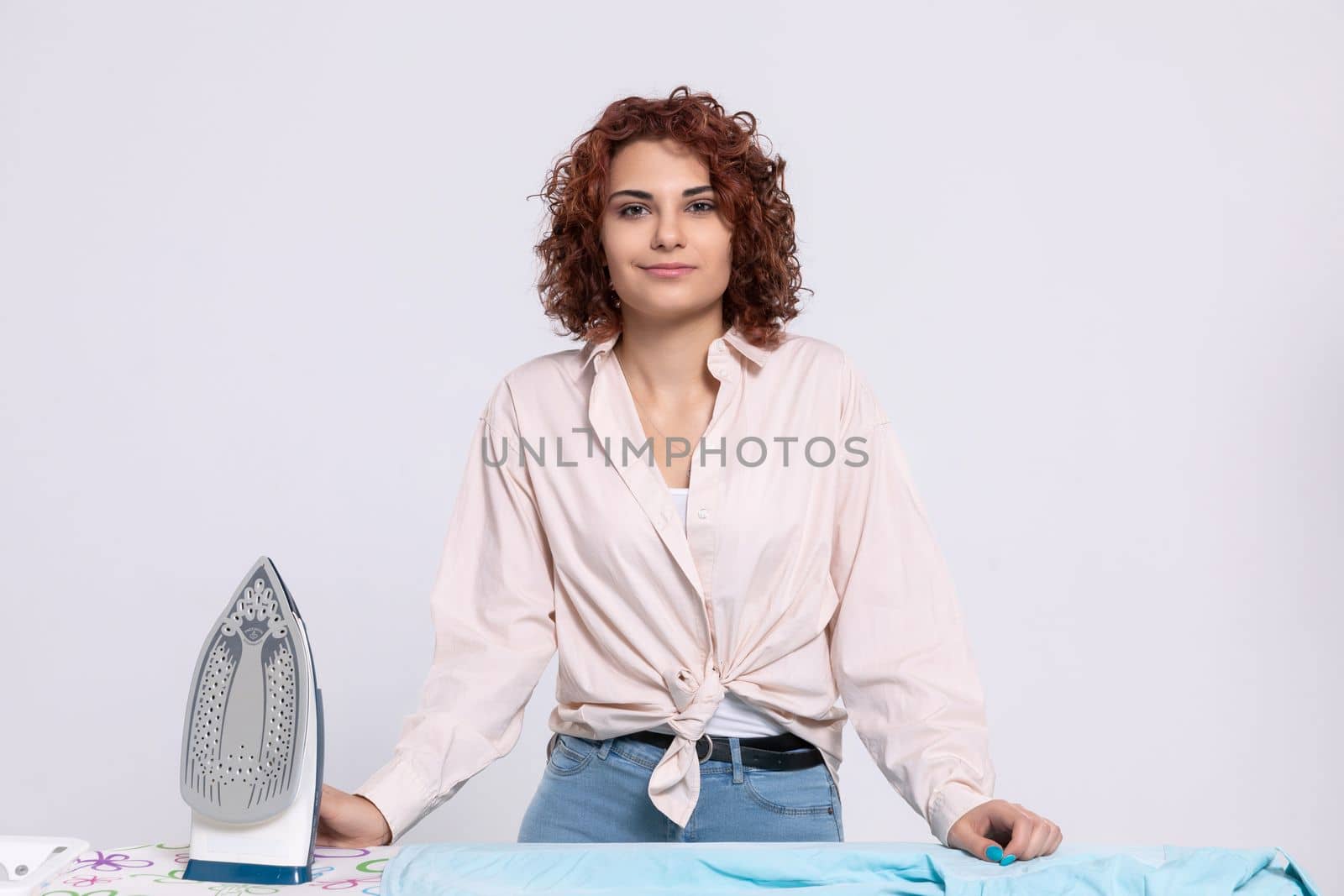 A girl with curly hair and a gentle smile on her face ready to start the daily ritual of ironing shirts. Natural hairstyle.